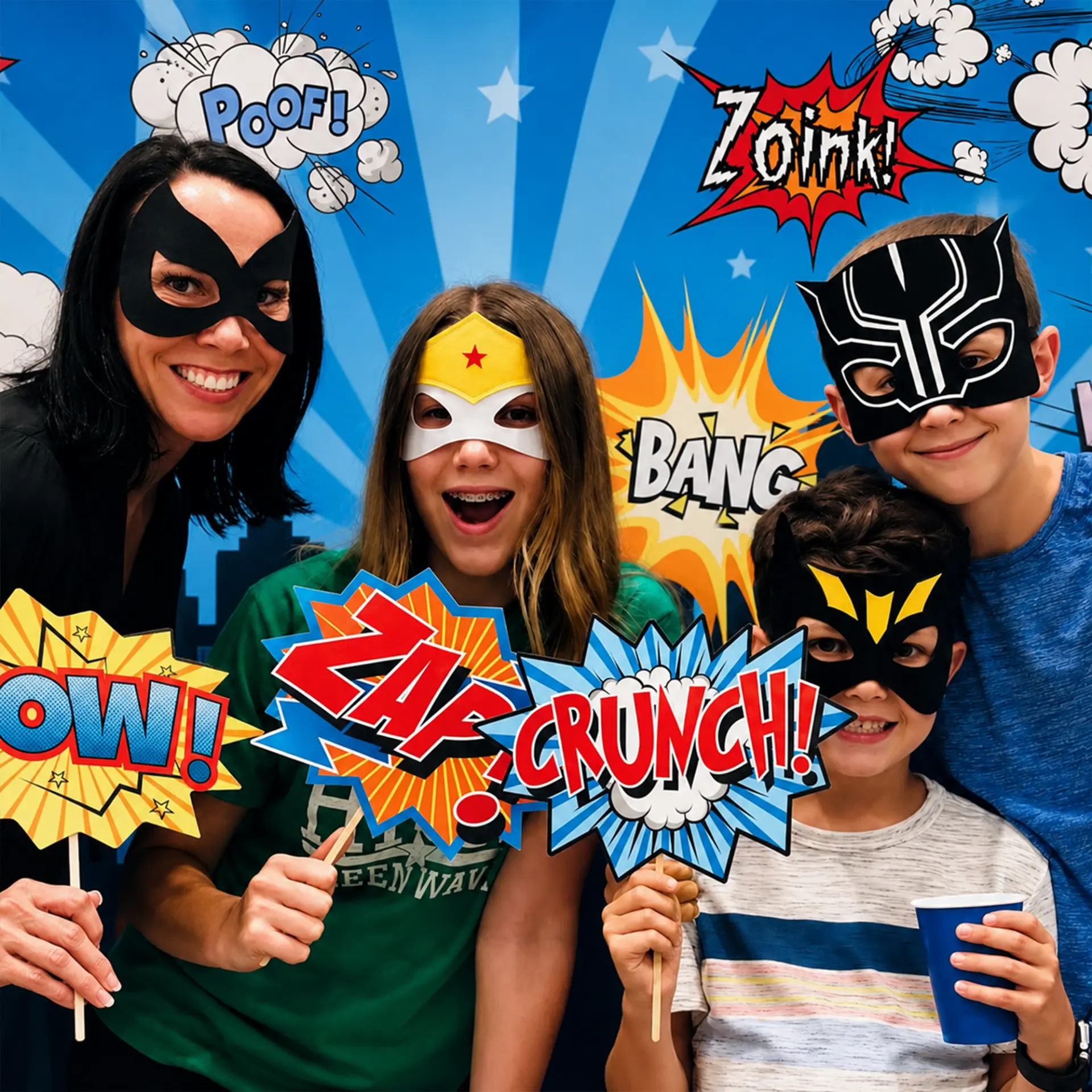 Family in superhero masks holding comic-book prop signs in front of a superhero backdrop